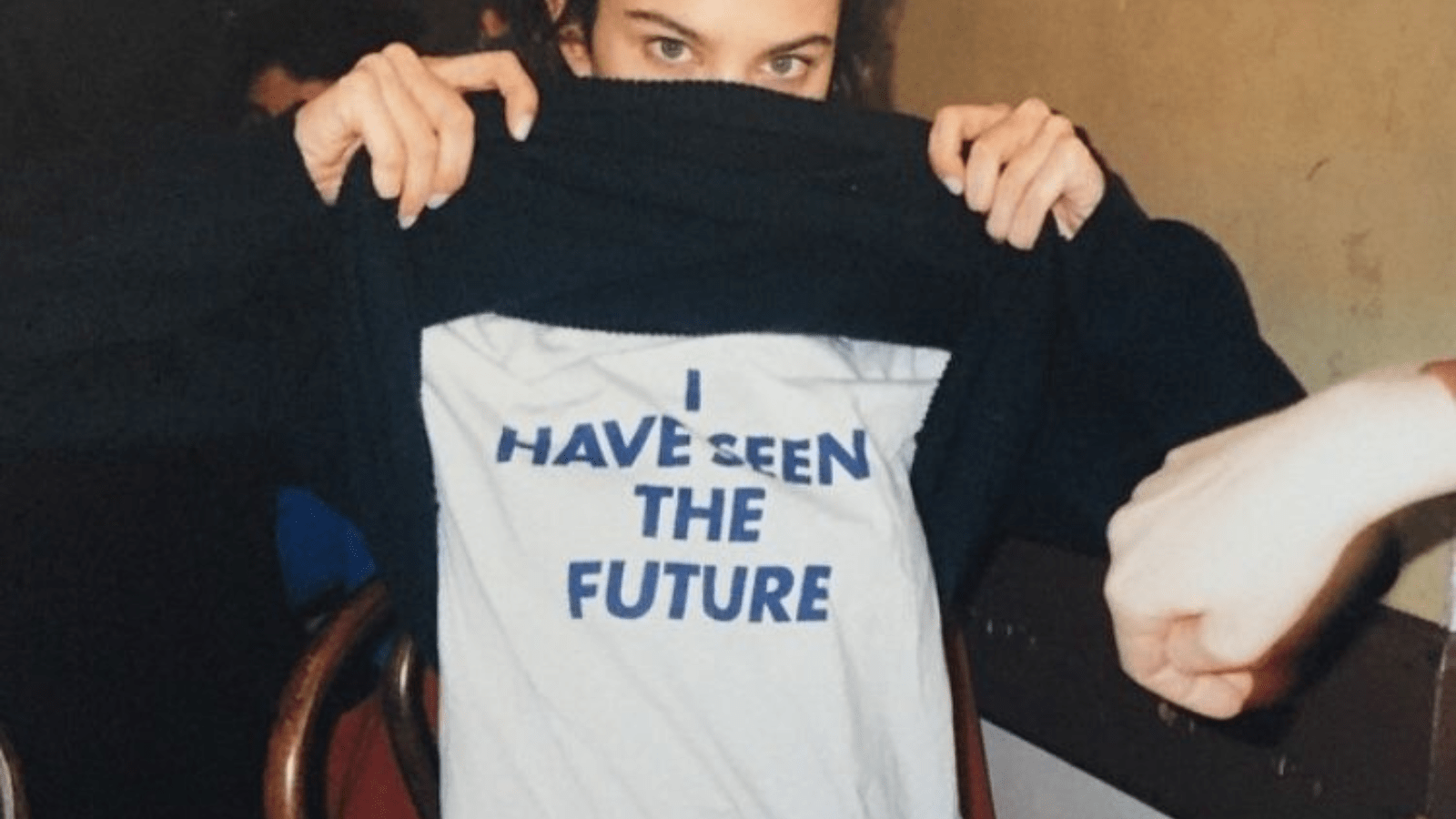 image depicting a eurasian woman alexa chung staring at the camera holding up her sweater to reveal a white t-shirt underneath with the slogan 'I have seen the future' in bold navy capital letters